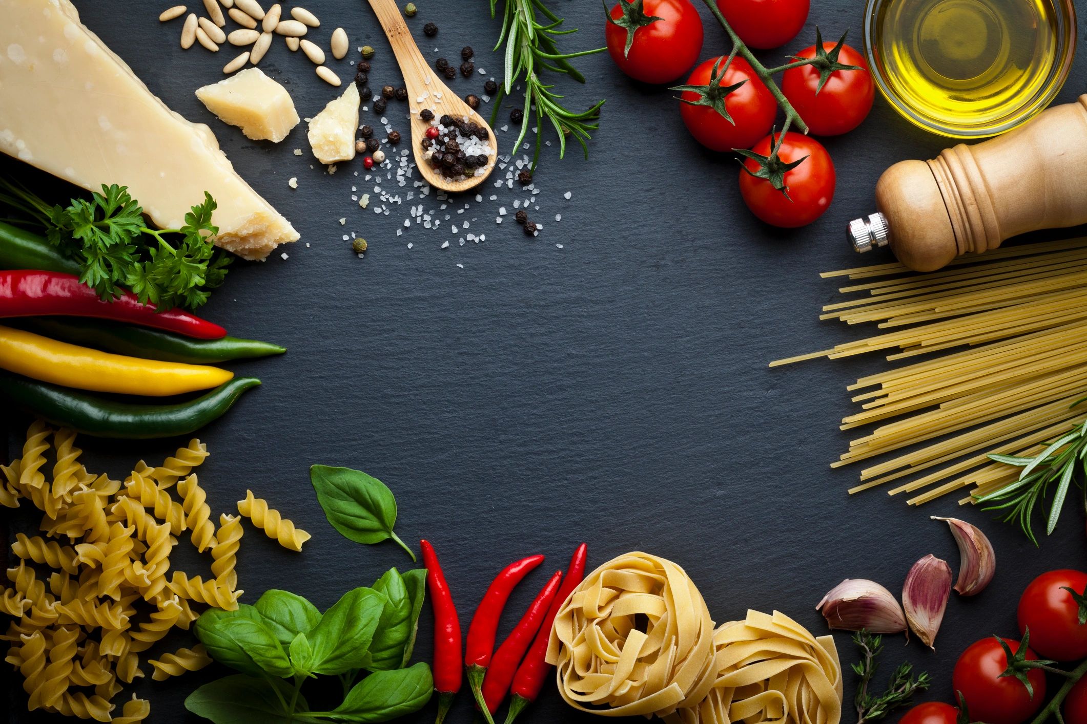 Pasta ingredients arranged on a dark stone background with copy space
